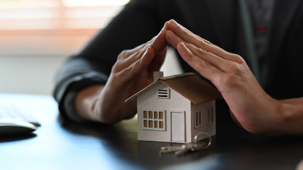 Cropped image of small house covered by hands. Property insurance concept.